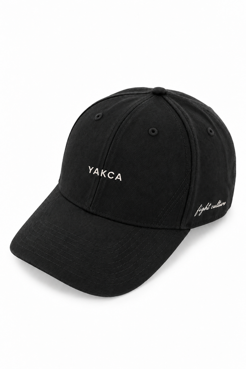 YAKCA CORE washed-black six-panel cap with small off-white YAKCA front embroidery, tonal curved stitching and fight culture script on the side